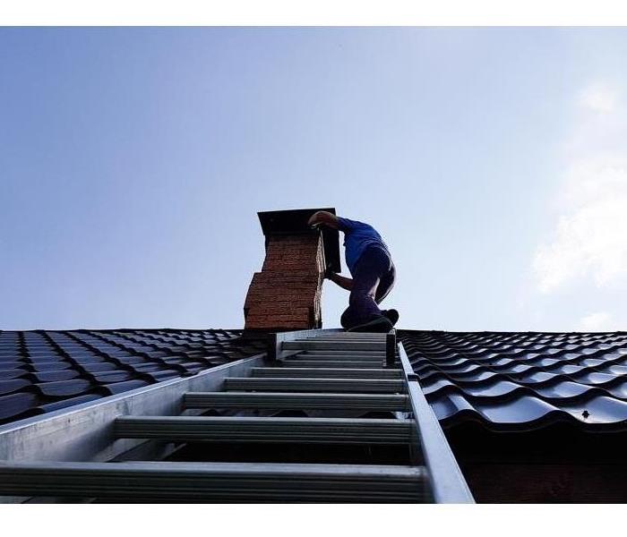A man cleans a chimney from the roof access point.
