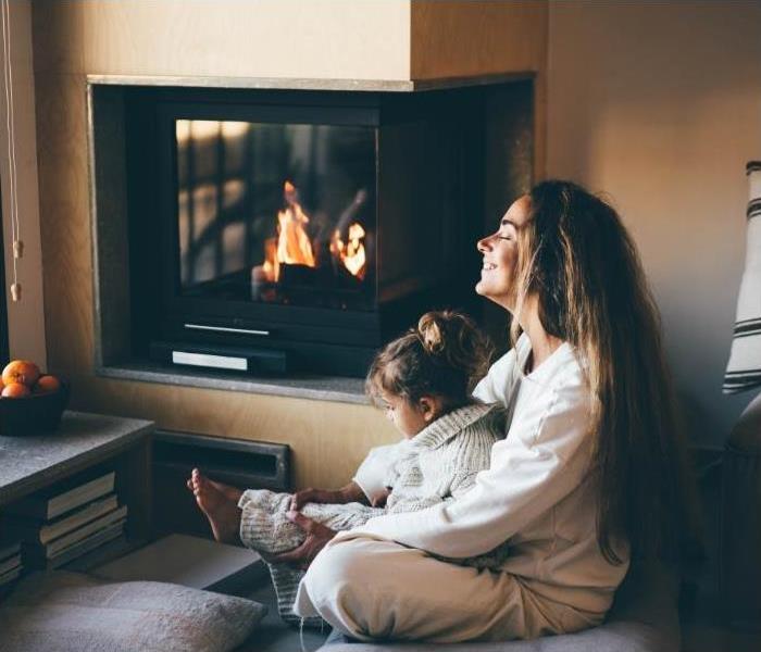 Mother and child sitting next to a fireplace.