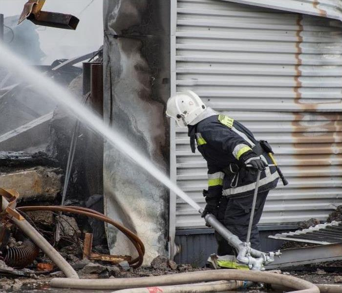 A firefighter directing a water hose into a fire damaged building.